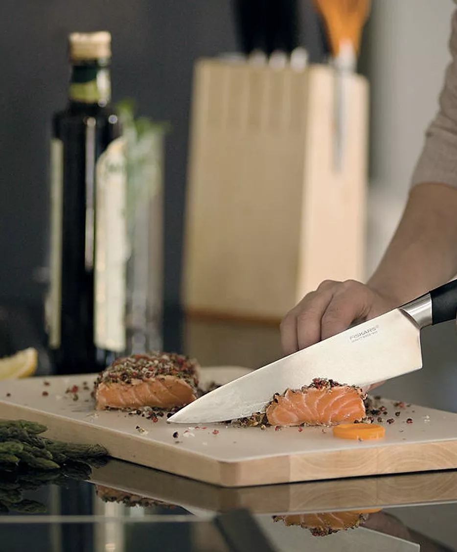 Chef slicing pepper-crusted salmon fillet on cutting board with kitchen knife, olive oil bottle in background