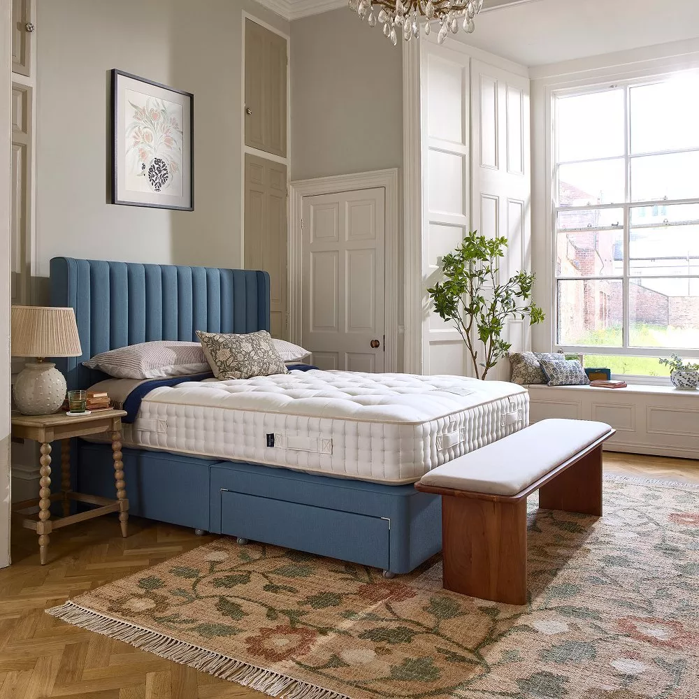 Bright modern bedroom with blue upholstered bed, white mattress, wooden bench, and large sash window light