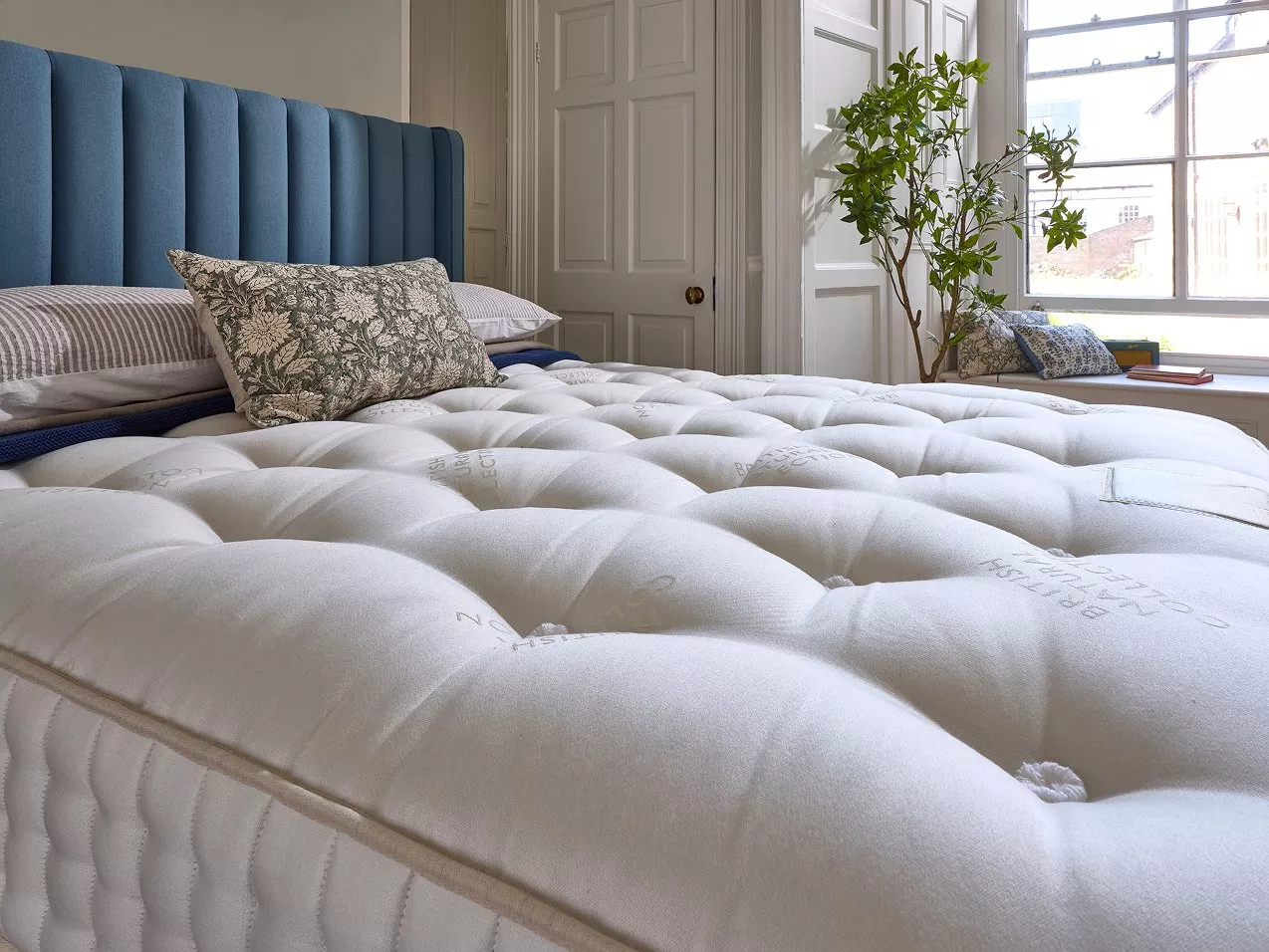 Luxury tufted mattress on bed with blue upholstered headboard in bright, modern bedroom by large window