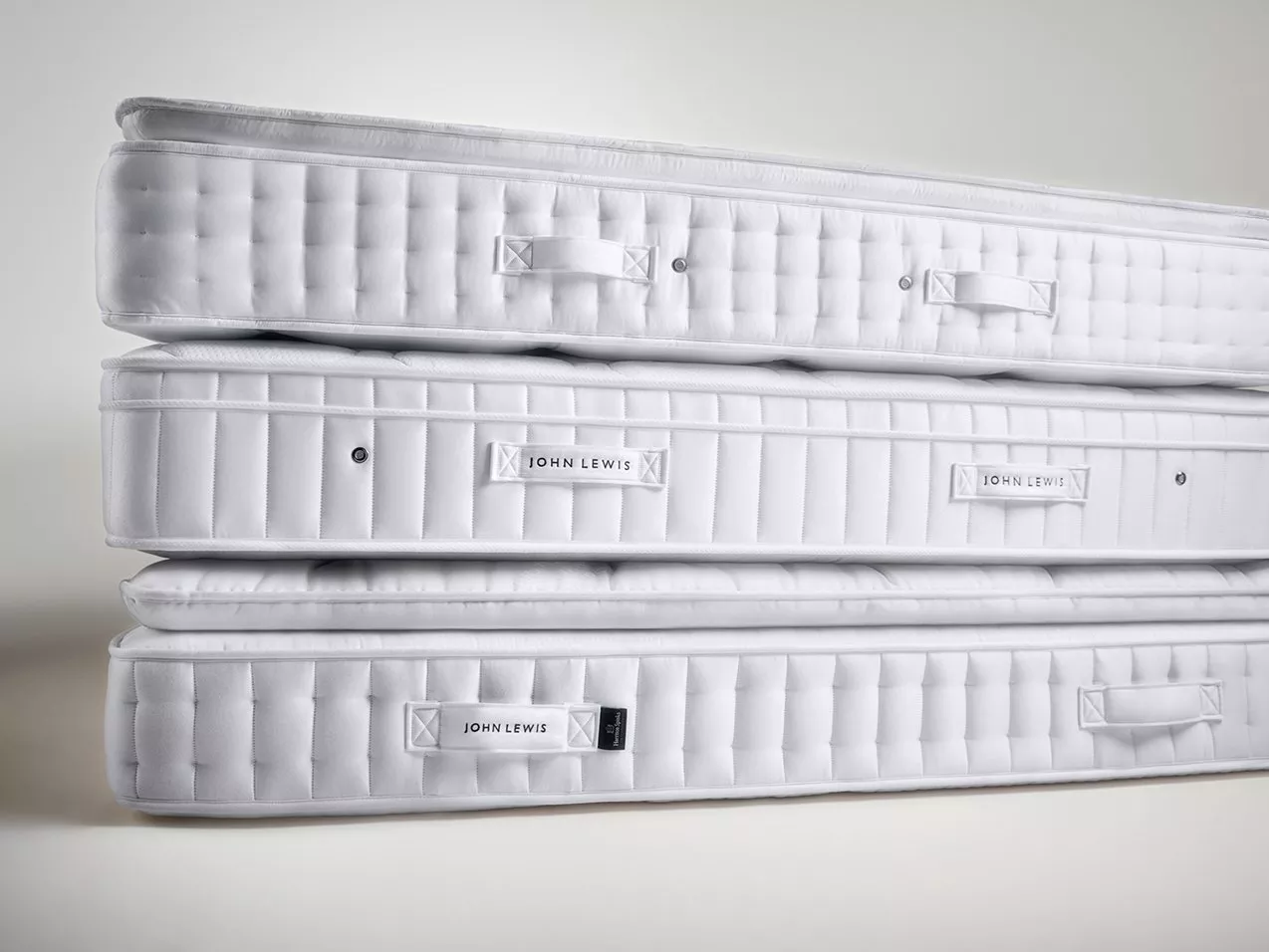 Stacked white John Lewis pocket spring mattresses with quilted sides and handles on a neutral studio background