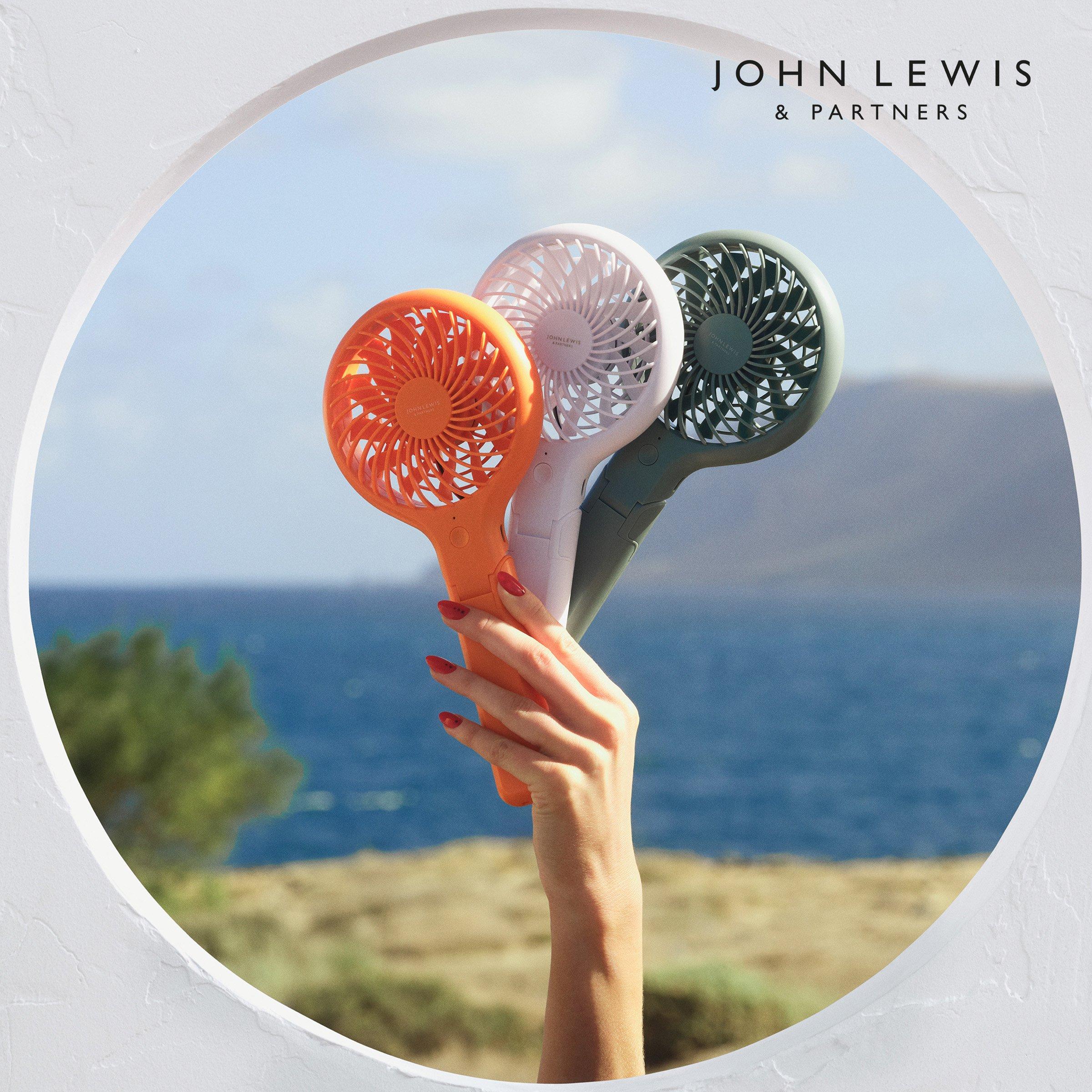 Hand holding three colorful portable fans against a sea background.