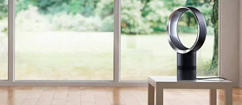 Modern bladeless tower fan on side table in bright living room, person using remote by large window view