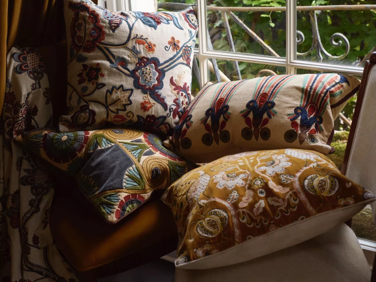 Stylish living room with a floral sofa, vibrant cushions, and an orange ottoman. A tray with flowers and books adds charm.