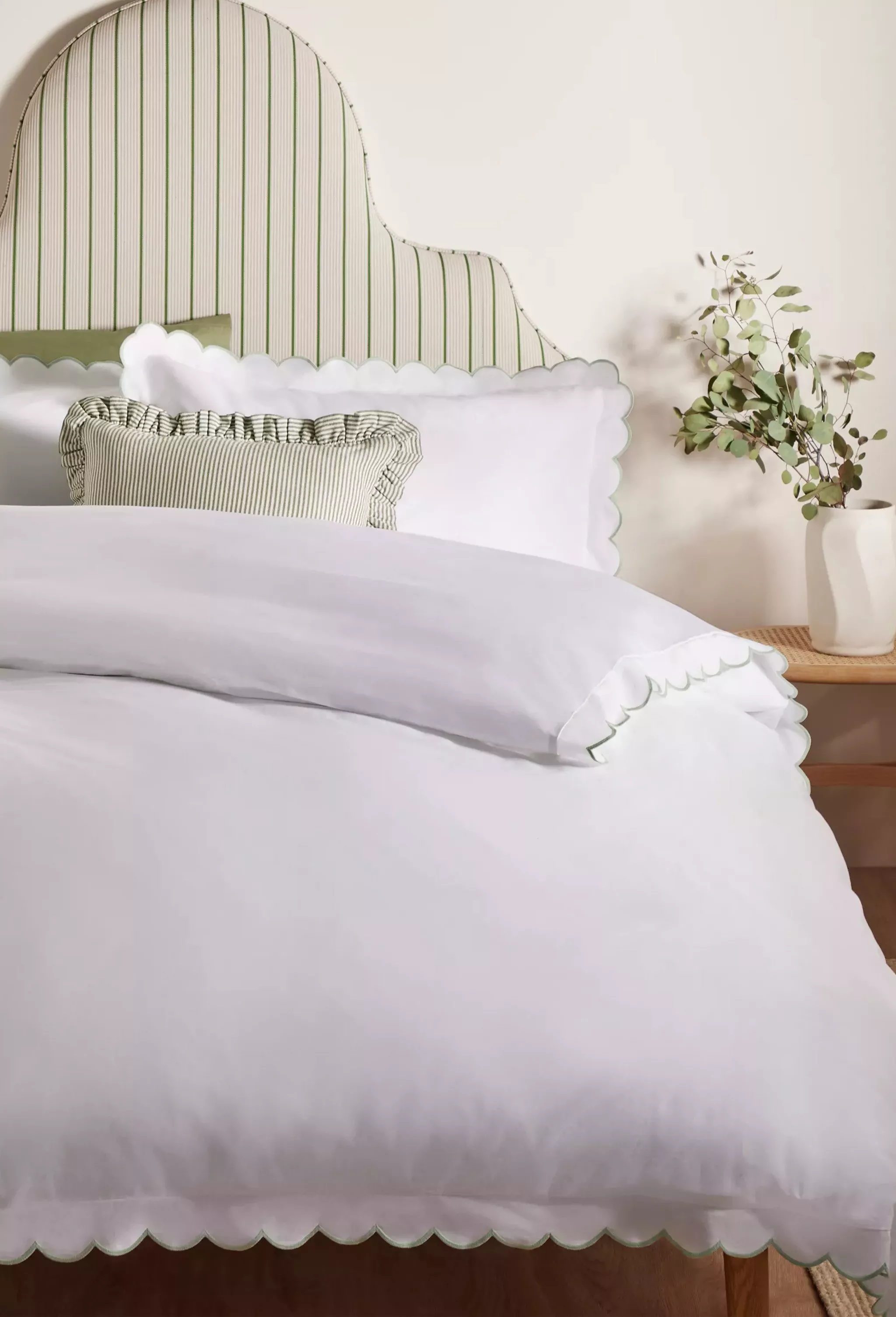 Tufted beige upholstered headboard with white bedding and grey throw in a modern bedroom interior.