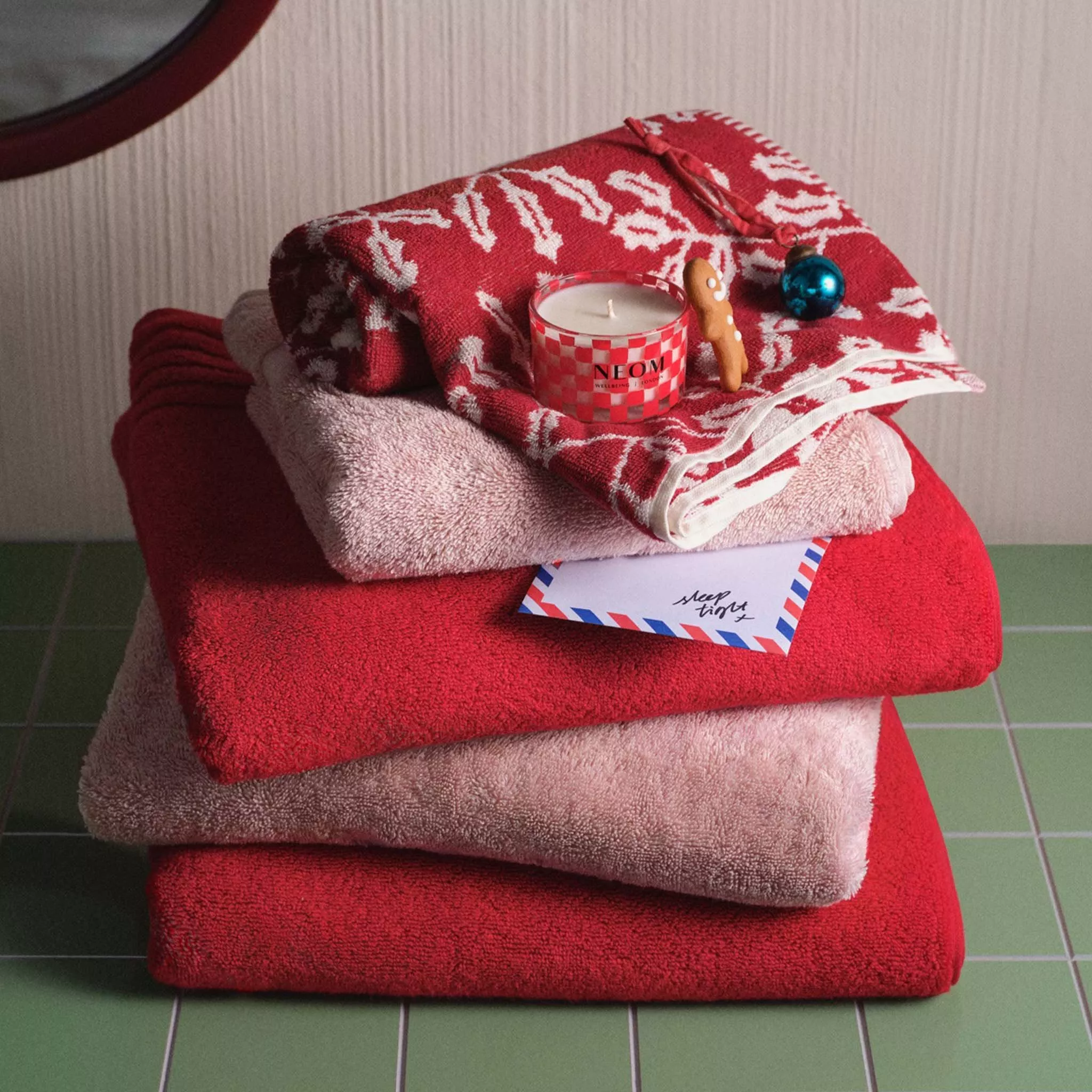 A stack of red and pink Christmas towels on green tiles 