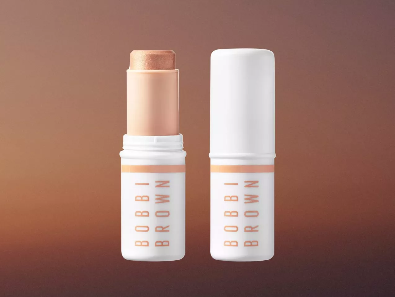 Bobbi Brown shimmer highlighter stick with cap off, alongside closed tube on warm brown background