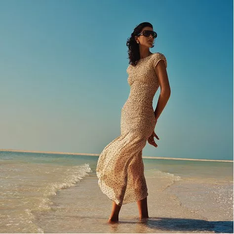 Elegant woman in polka dot maxi dress and sunglasses standing in shallow sea, summer beach fashion photo