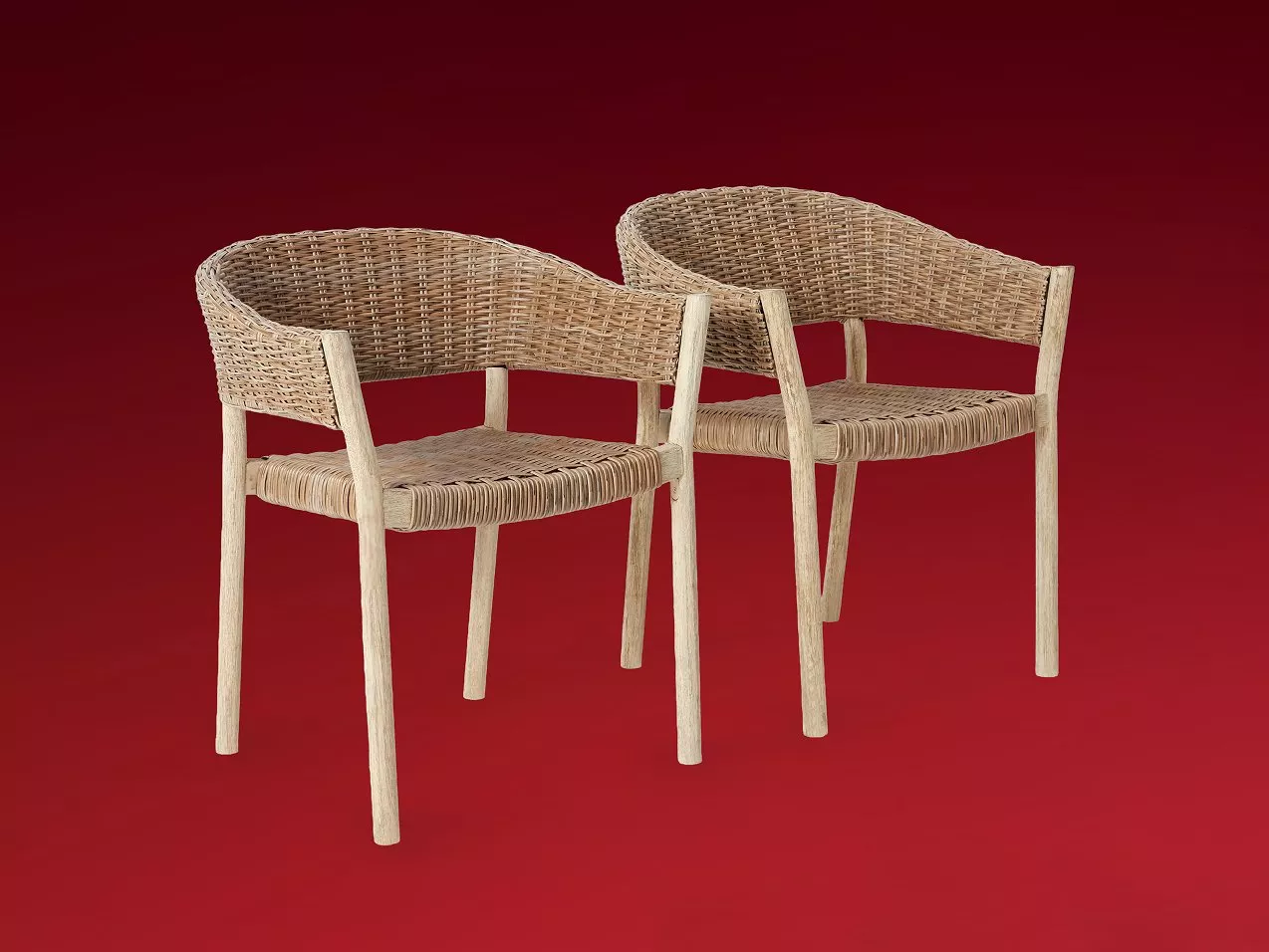 Pair of natural rattan dining chairs with woven seats and curved backs, light wood legs on red backdrop