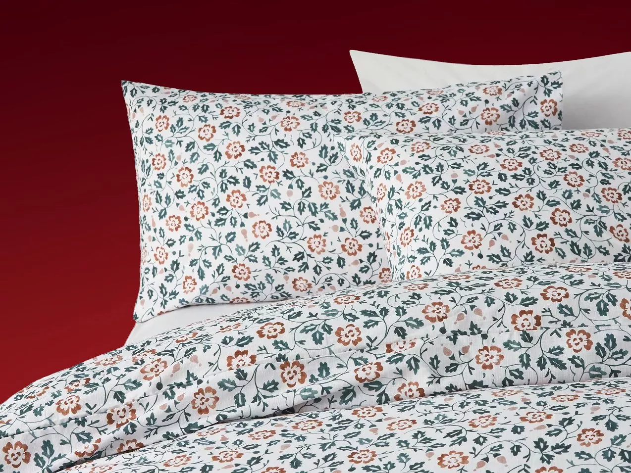 Floral duvet cover and pillowcases with green leaves and terracotta flowers on white bed linen with a red backdrop