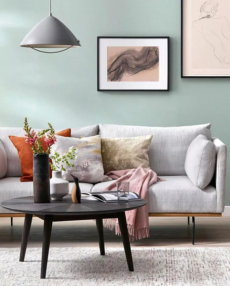 Modern living room with grey sofa, colourful cushions, and sleek coffee table. Art decorates the pale green walls.