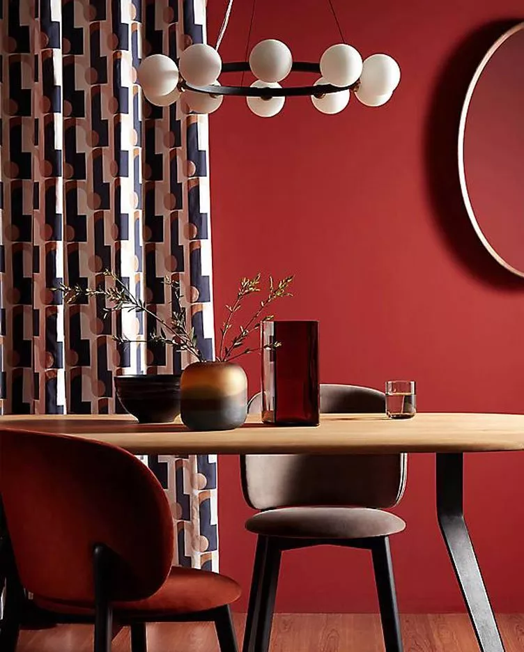 Stylish dining room with red walls, patterned curtains, modern chandelier, and elegant table decor.