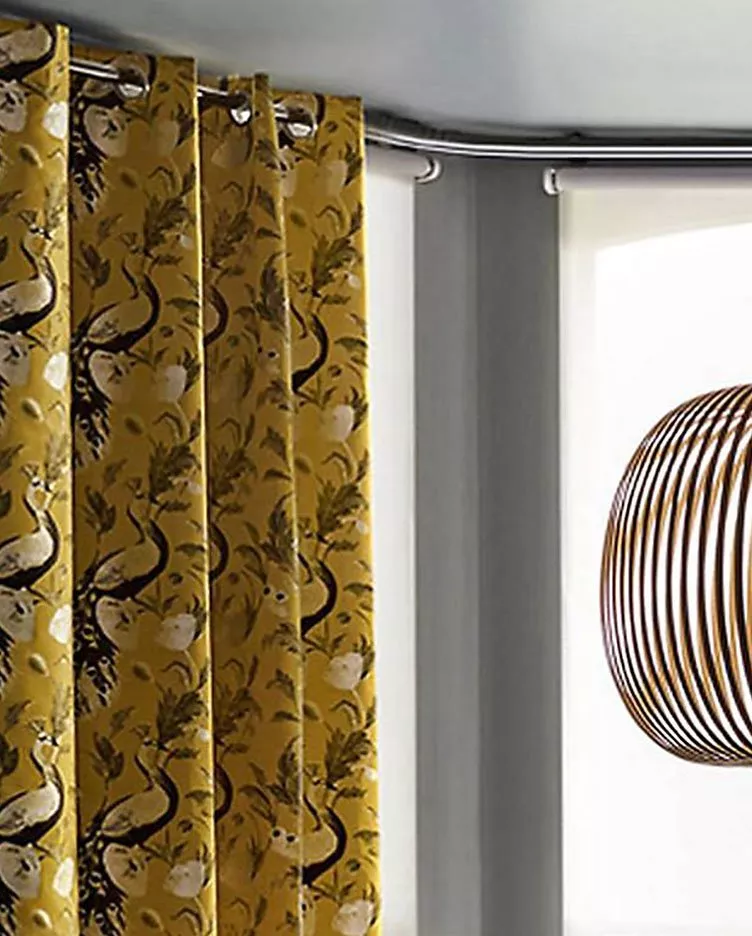 Yellow floral curtains hang beside a window with a modern pendant light featuring curved wooden slats.