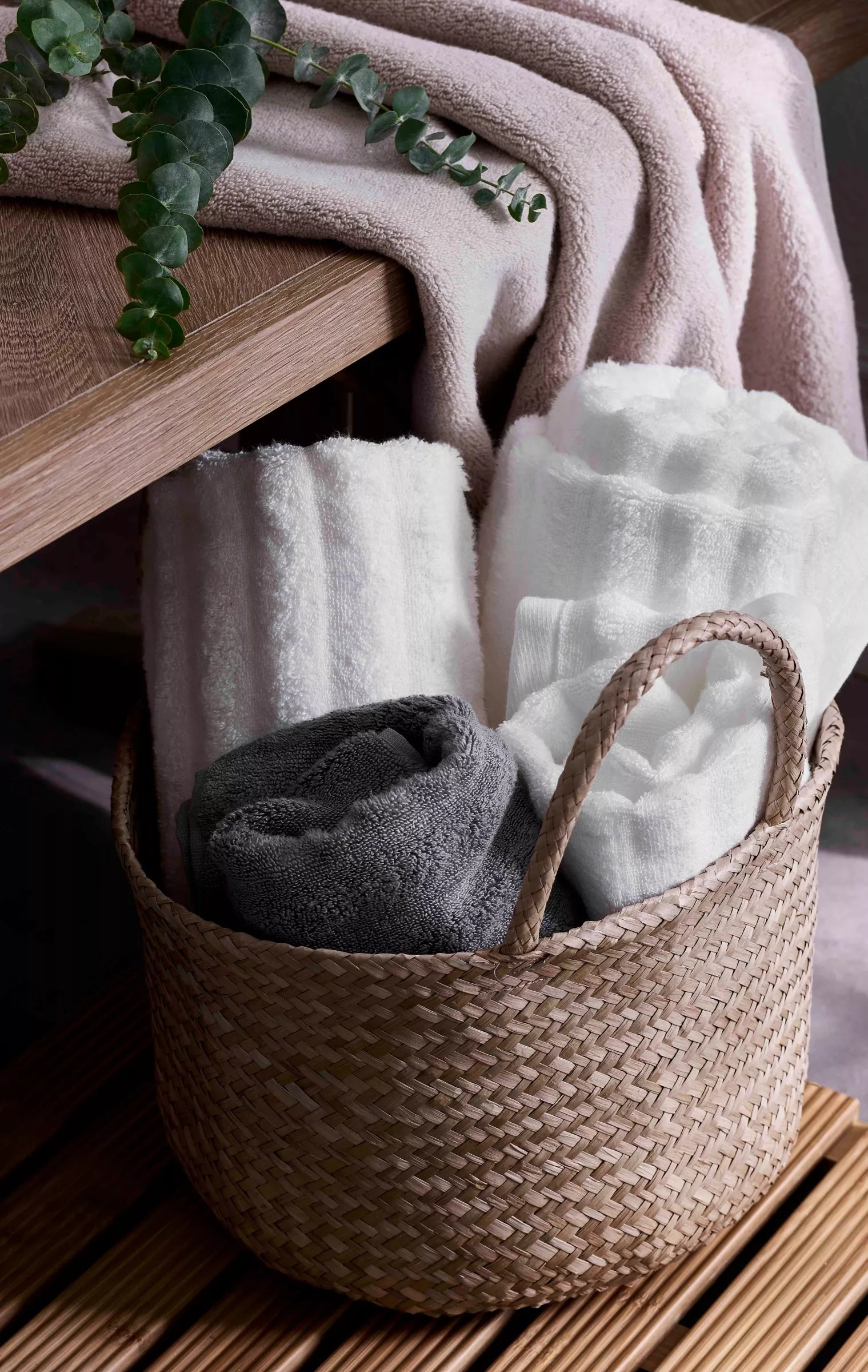 Neatly folded bath towels stacked on a wooden stool in a bright, modern bathroom with natural light