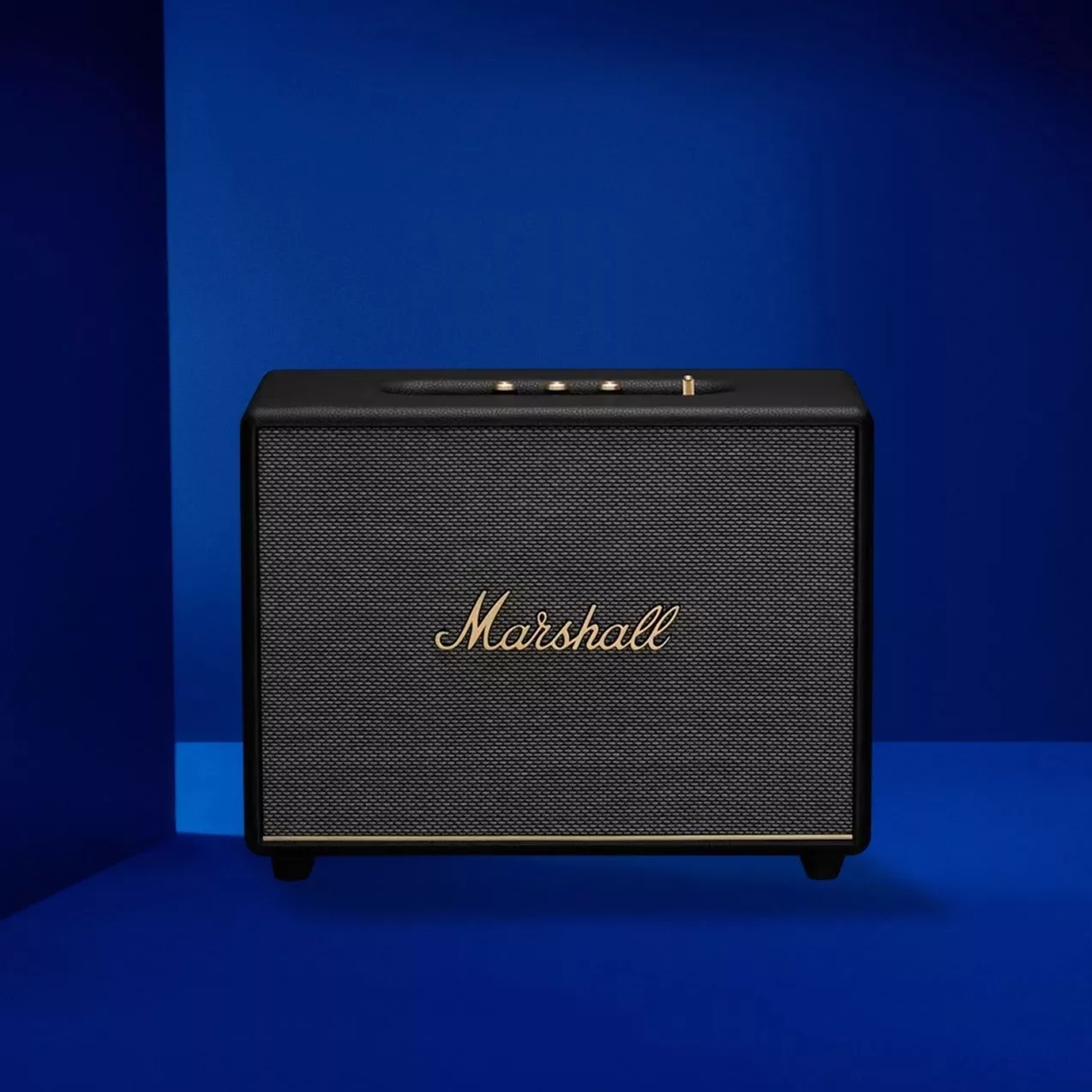 Marshall wireless Bluetooth speaker in black with gold logo, front view on a blue studio background