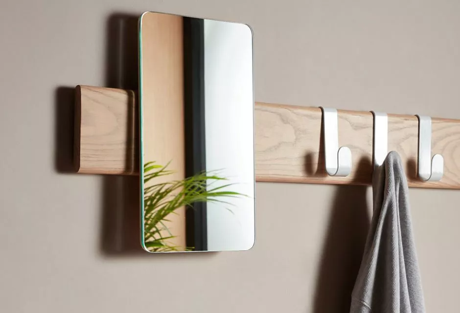 Modern wall mirror with wooden coat rack and metal hooks, grey towel hanging in minimalist hallway