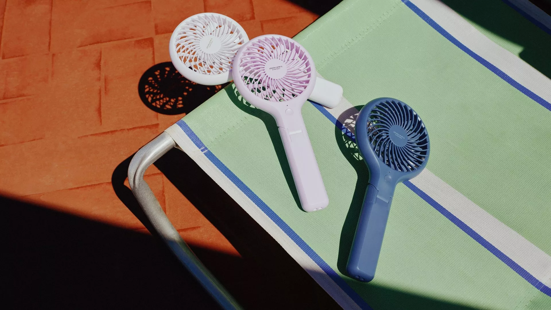 Three handheld portable mini fans on a striped sun lounger