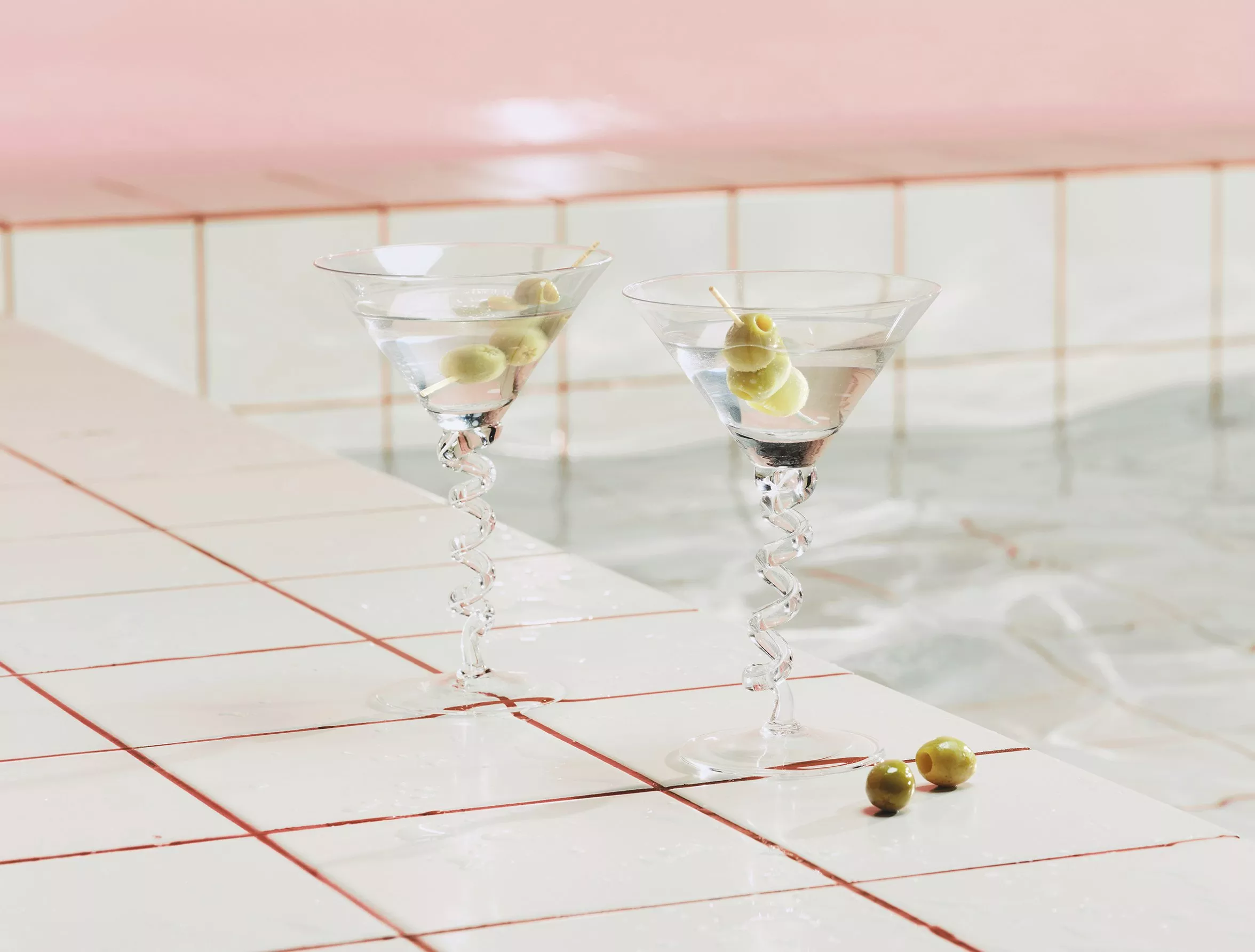 Two cocktail glasses at the side of a swimming pool