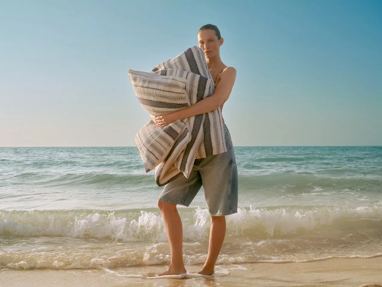 Woman standing on sandy beach holding striped quilted throw