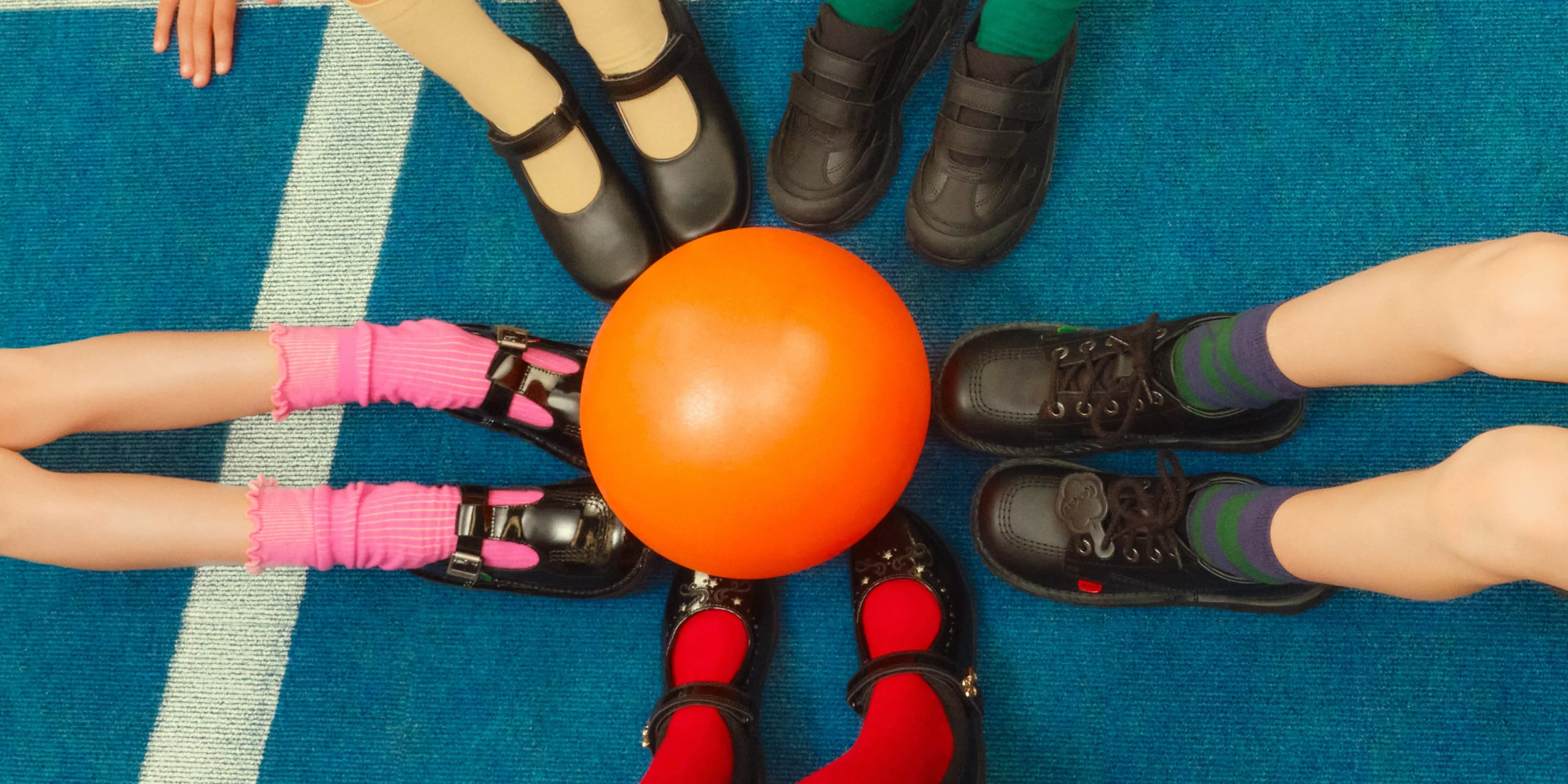 Children’s feet in school shoes around an orange ball on a blue carpet
