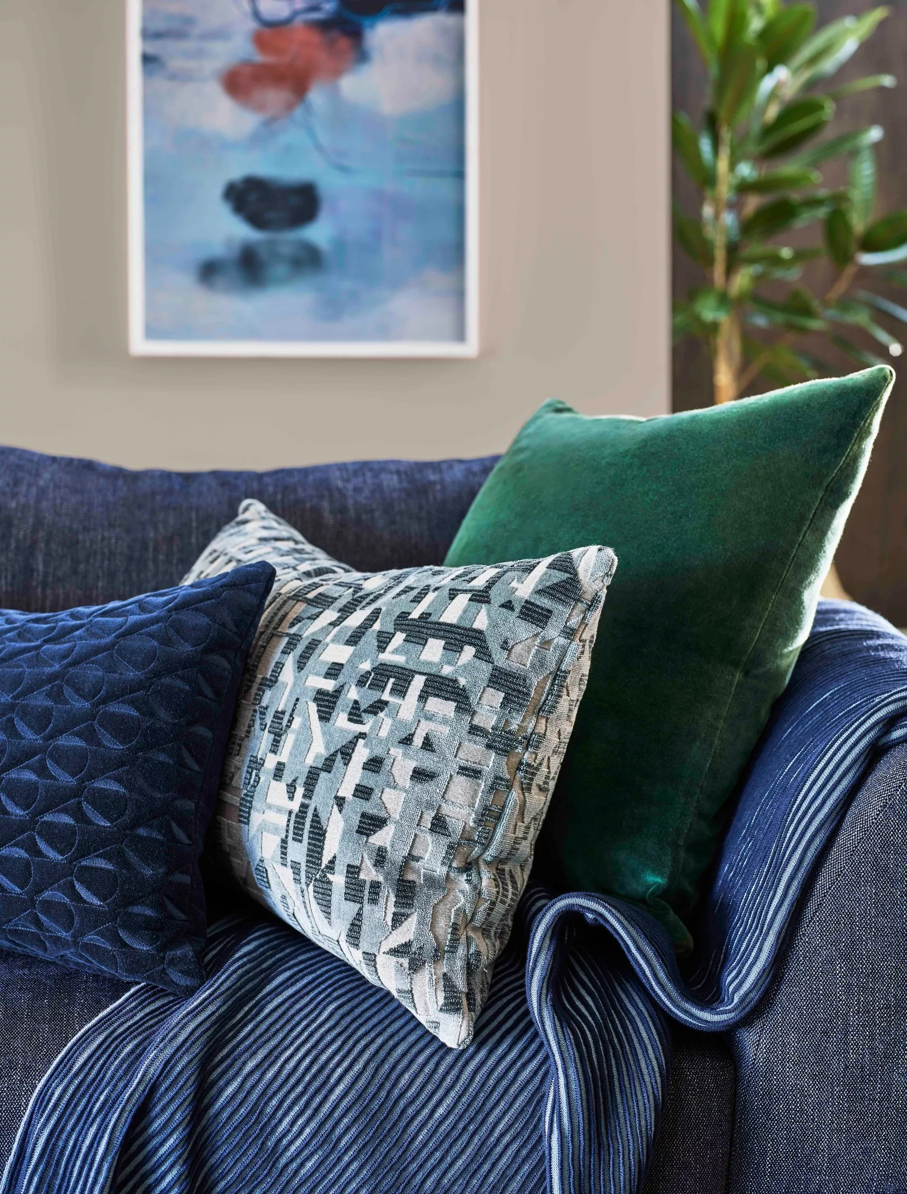 Blue sofa with patterned and green velvet cushions, styled living room corner with framed art and plant