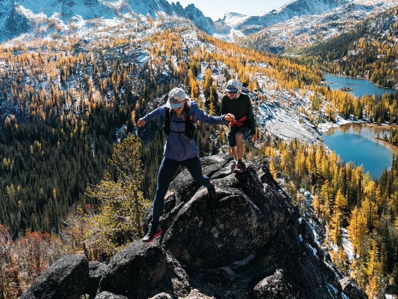 Two hikers climbing rocky mountain ridge above alpine lake and autumn forest, enjoying scenic outdoor adventure in highlands