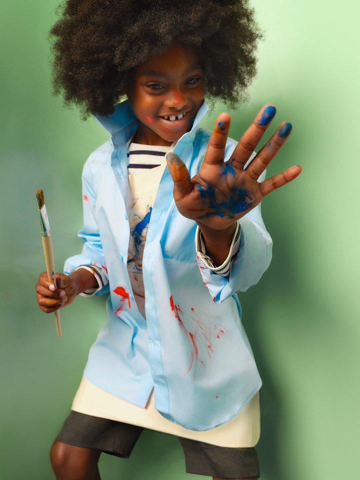 Girl wearing school uniform holding a paintbrush with paint on her hand