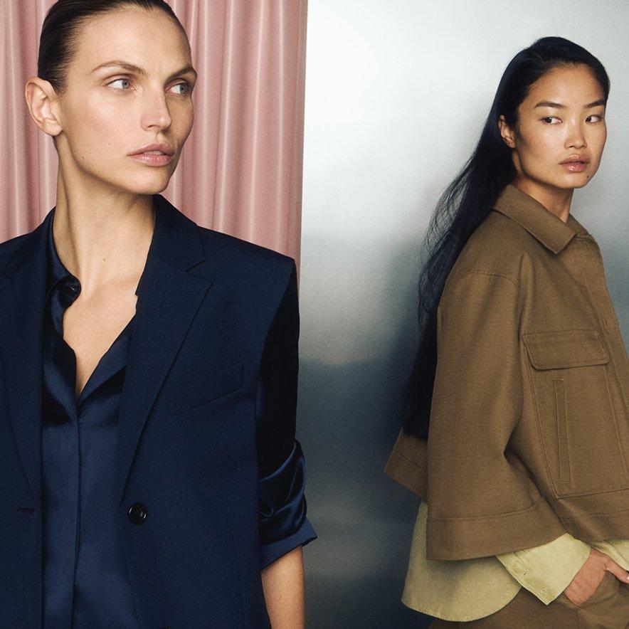 Two female models wearing a navy suit and a khaki jacket and light green shirt