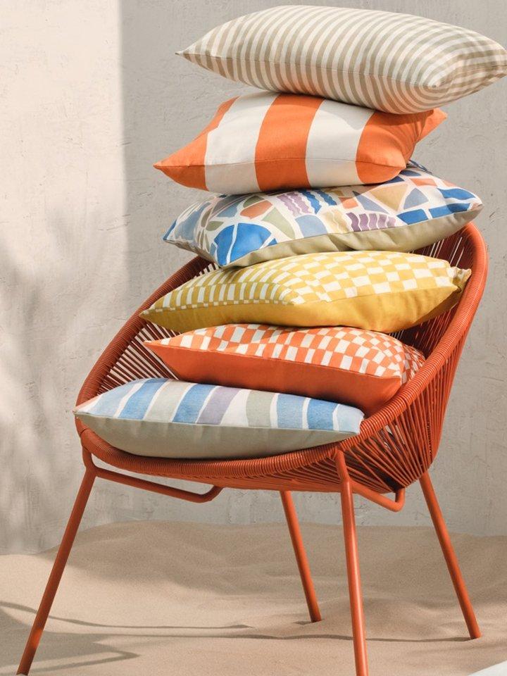 Selection of colourful garden cushions stacked on an orange garden chair