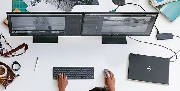 Overhead view of video editor workstation with dual monitors, keyboard, mouse and laptop on white desk
