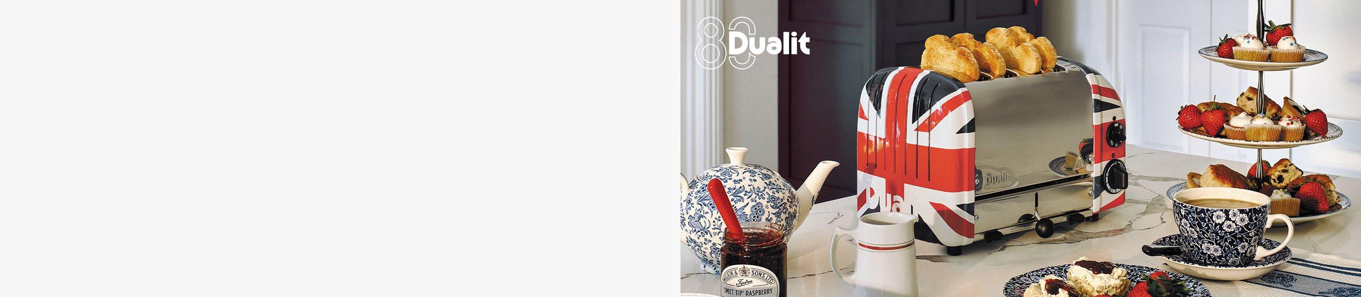 Dualit Union Jack classic toaster next to a cup of tea and a cake stand with strawberries and cupcakes