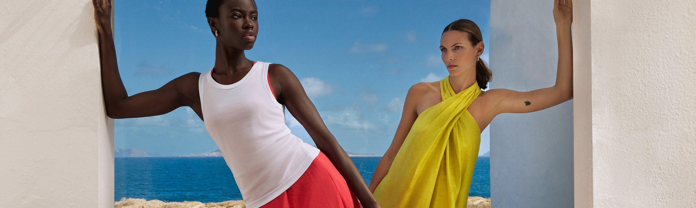 Two female models wearing summer dresses with the sea in the background