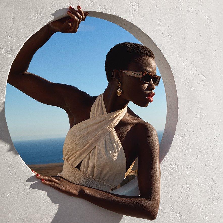 Female model wearing summer dress and sunglasses with the sea in the background