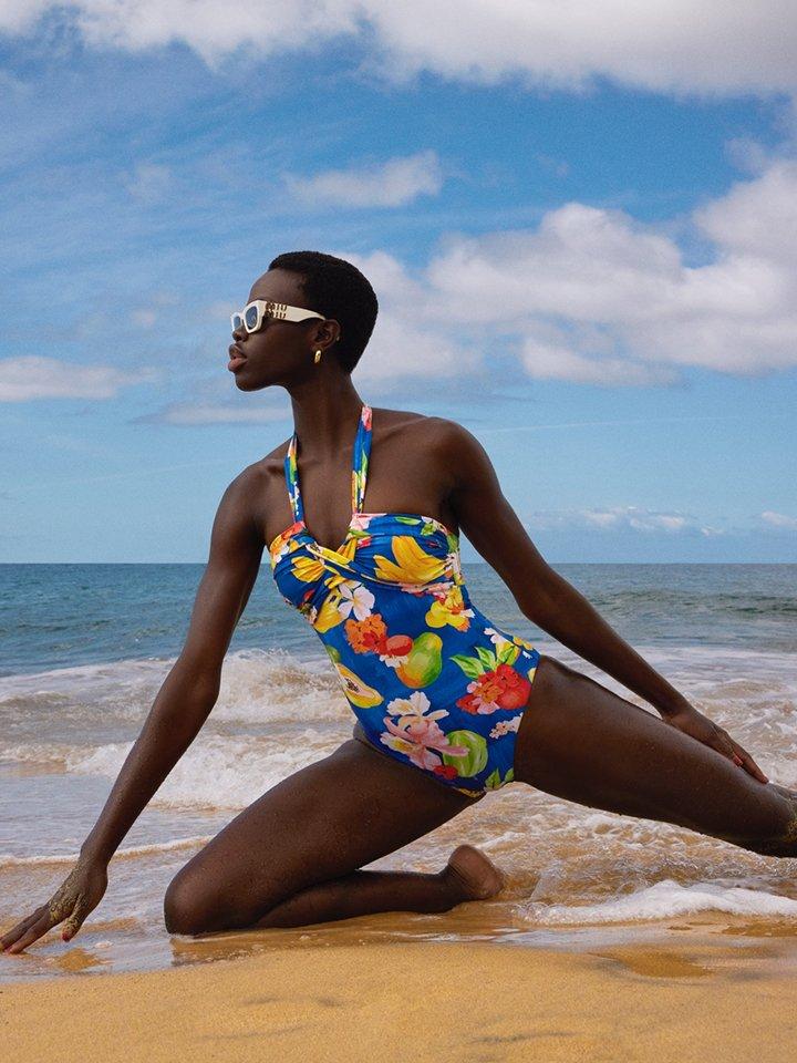 A female model posing on a coastline, wearing a bright blue, boldly patterned swimsuit
