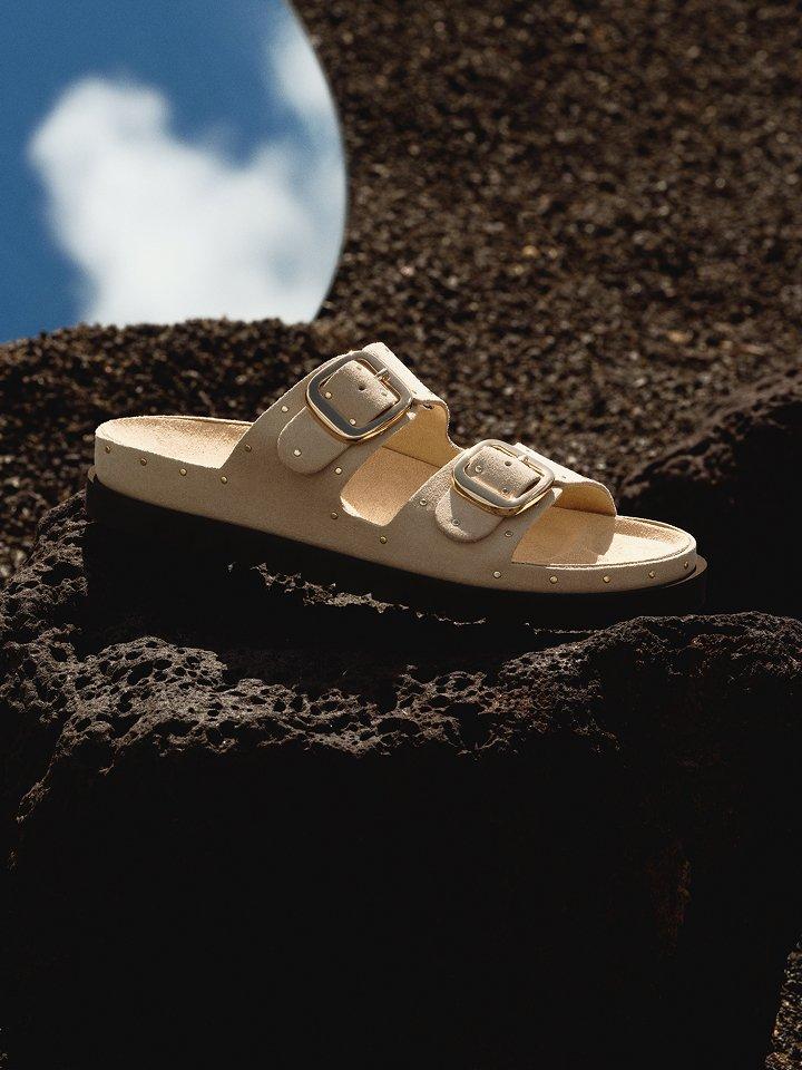 A women’s sandal displayed on black rock.