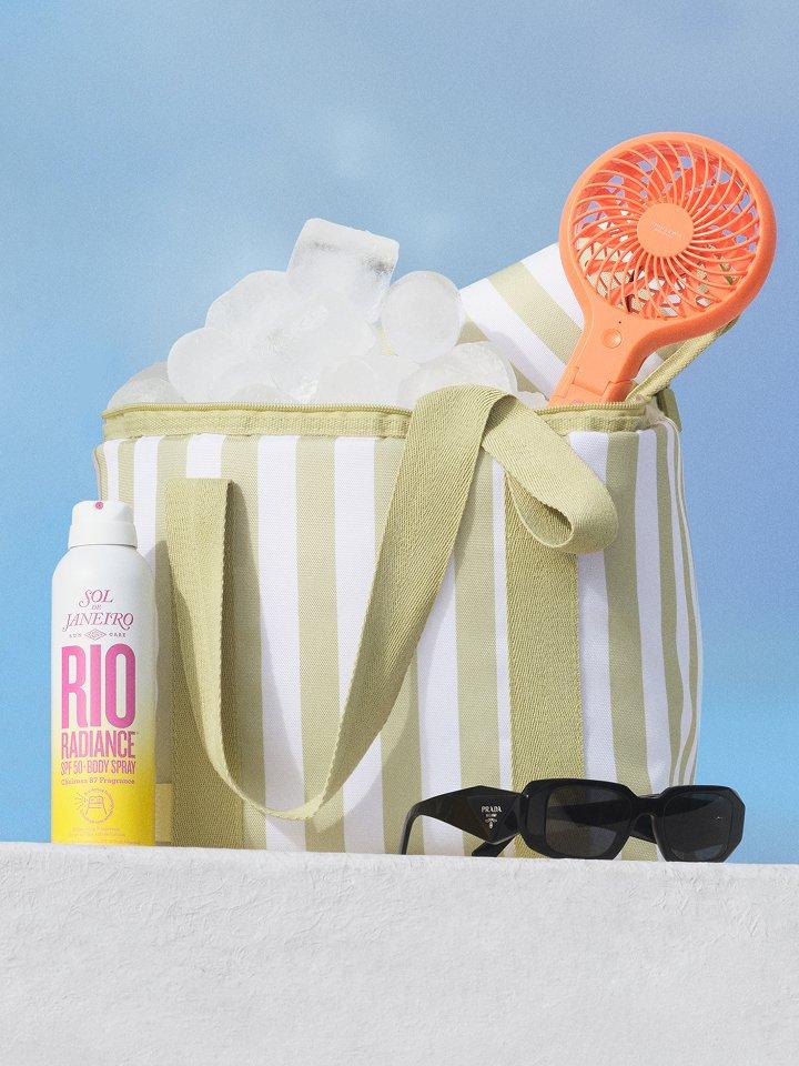 Festival essentials, including a striped cooler bag, a portable fan, and sunglasses, are on display outside