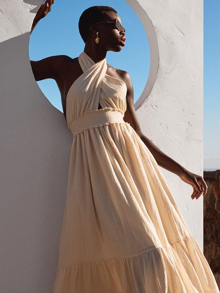 A female model is standing outside wearing a cream-coloured long dress