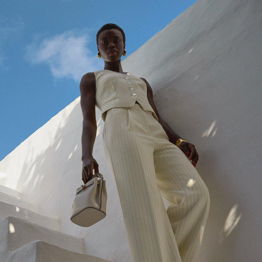 Female model posing outdoors in a white striped sleeveless trouser co-ord, holding a handbag