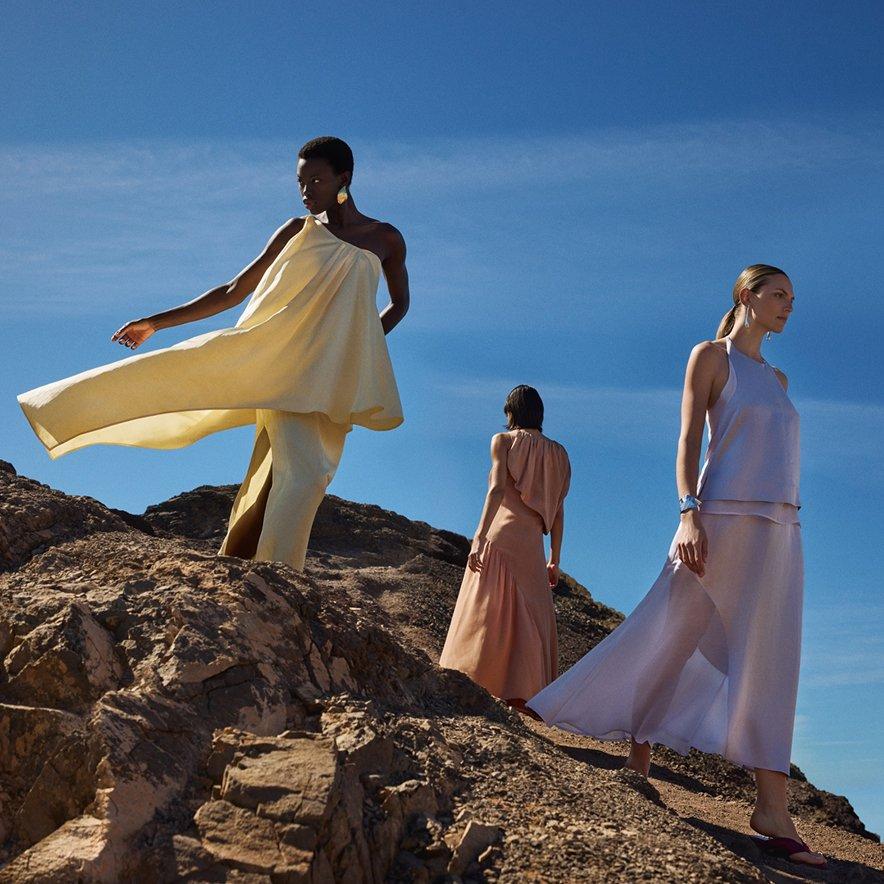 Three female models standing on rocks, dressed in pastel-coloured wedding guest outfits