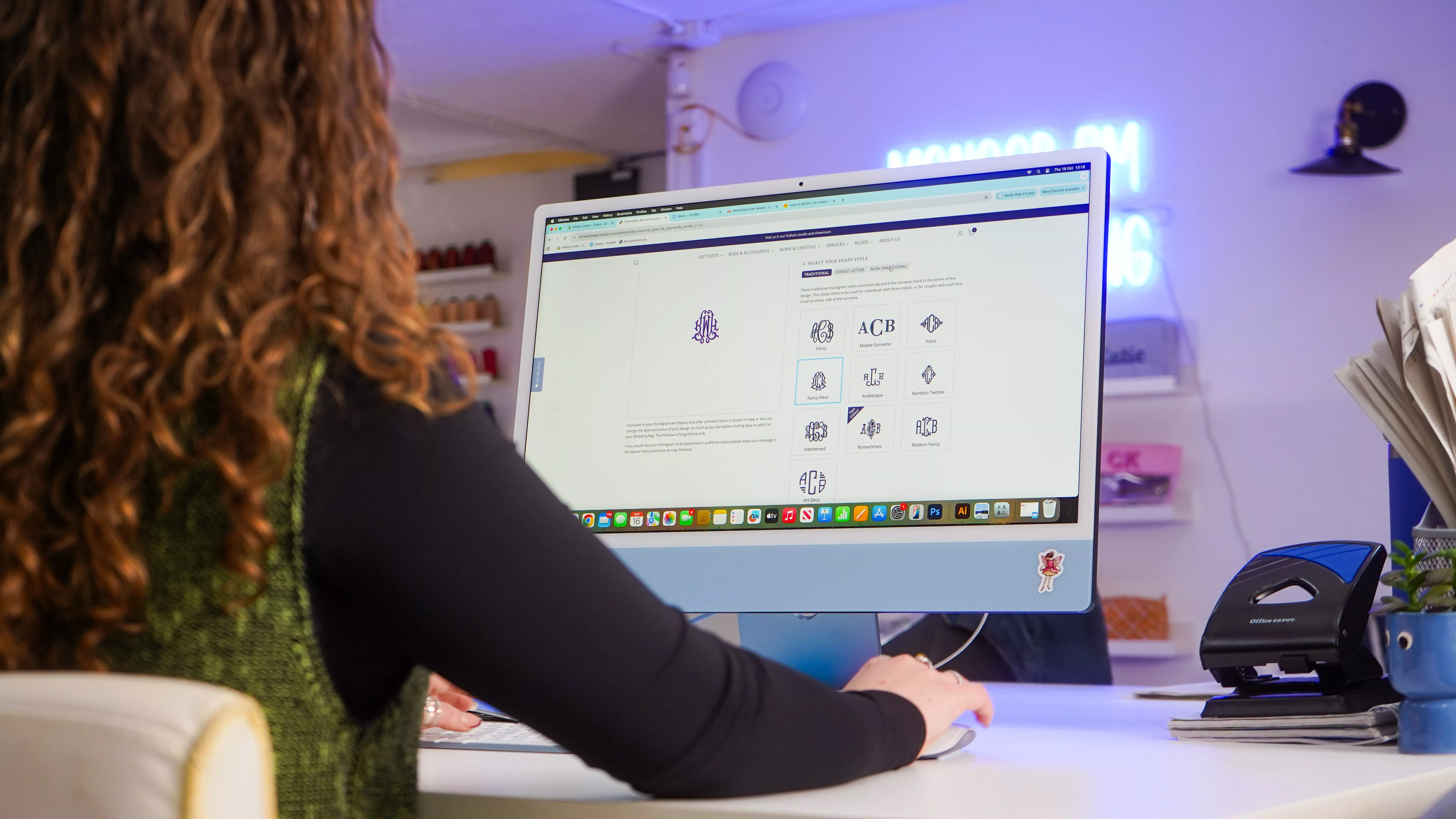 Woman using desktop computer to design a personalised monogram logo in a small creative studio workspace.