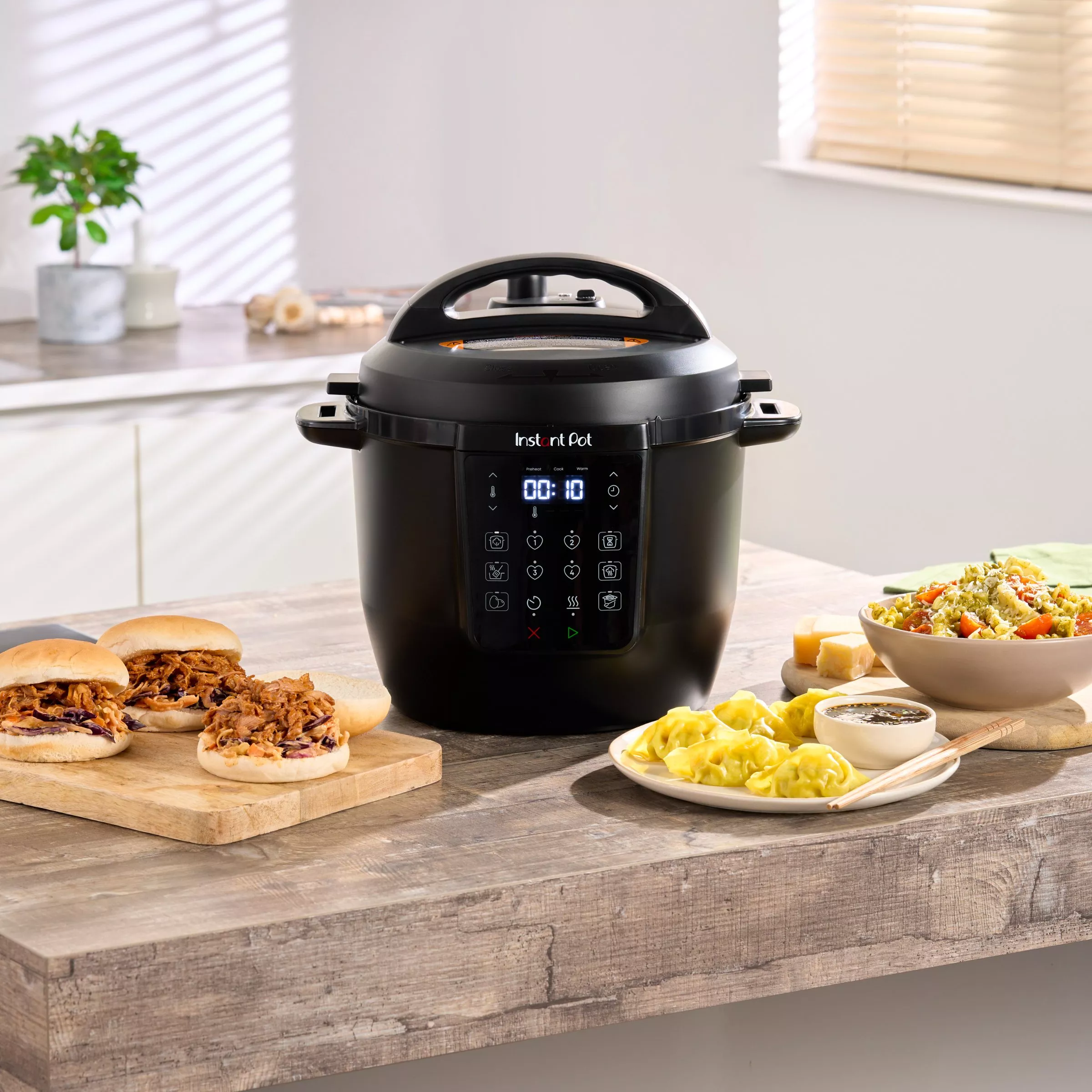 Instant Pot electric pressure cooker on kitchen counter with pulled pork rolls, dumplings and salad sides