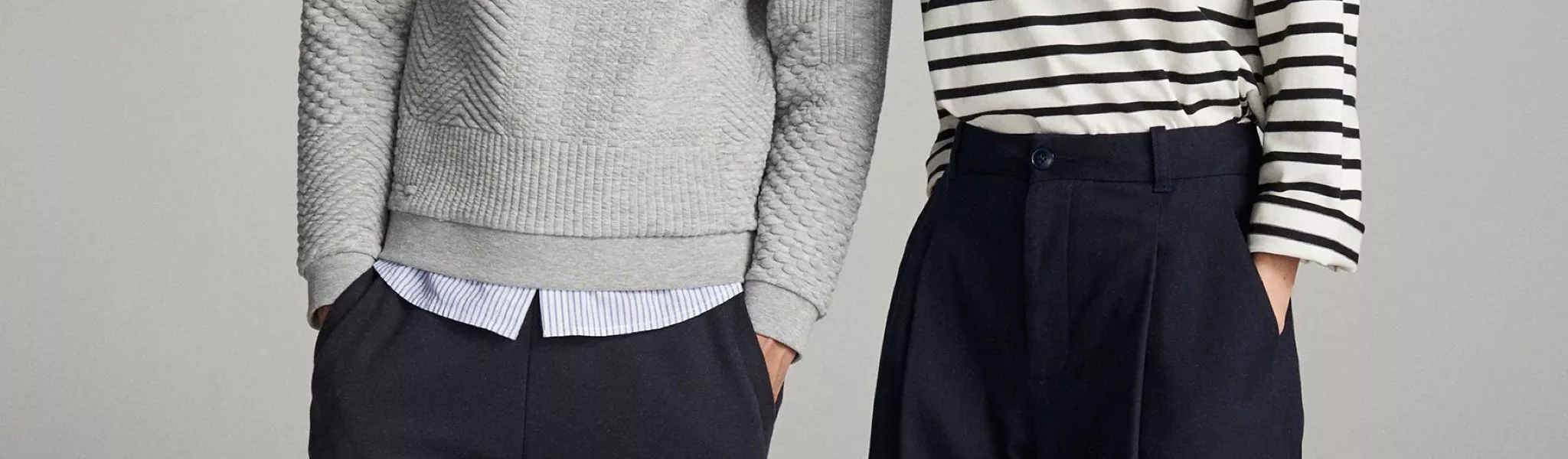 Two models wearing smart casual outfits with striped top, textured jumper and tailored navy trousers, studio shot