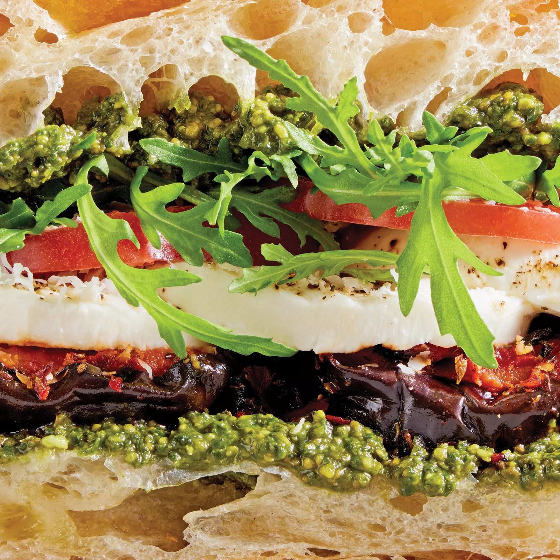 Close-up of focaccia sandwich with mozzarella, aubergine, pesto, rocket and tomato, gourmet lunch filling