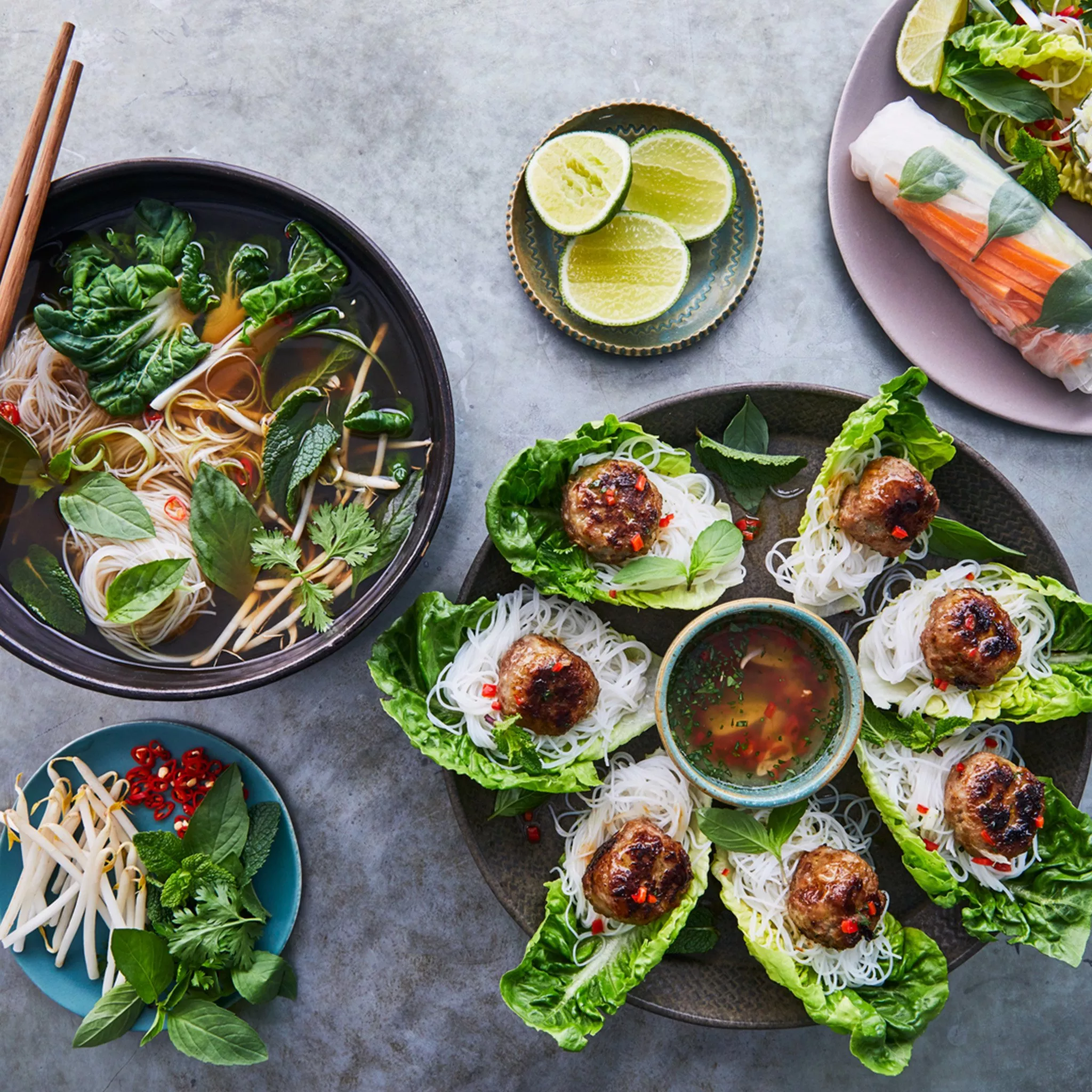 A table with Vietnamese food including a bowl of Pho and spring rolls