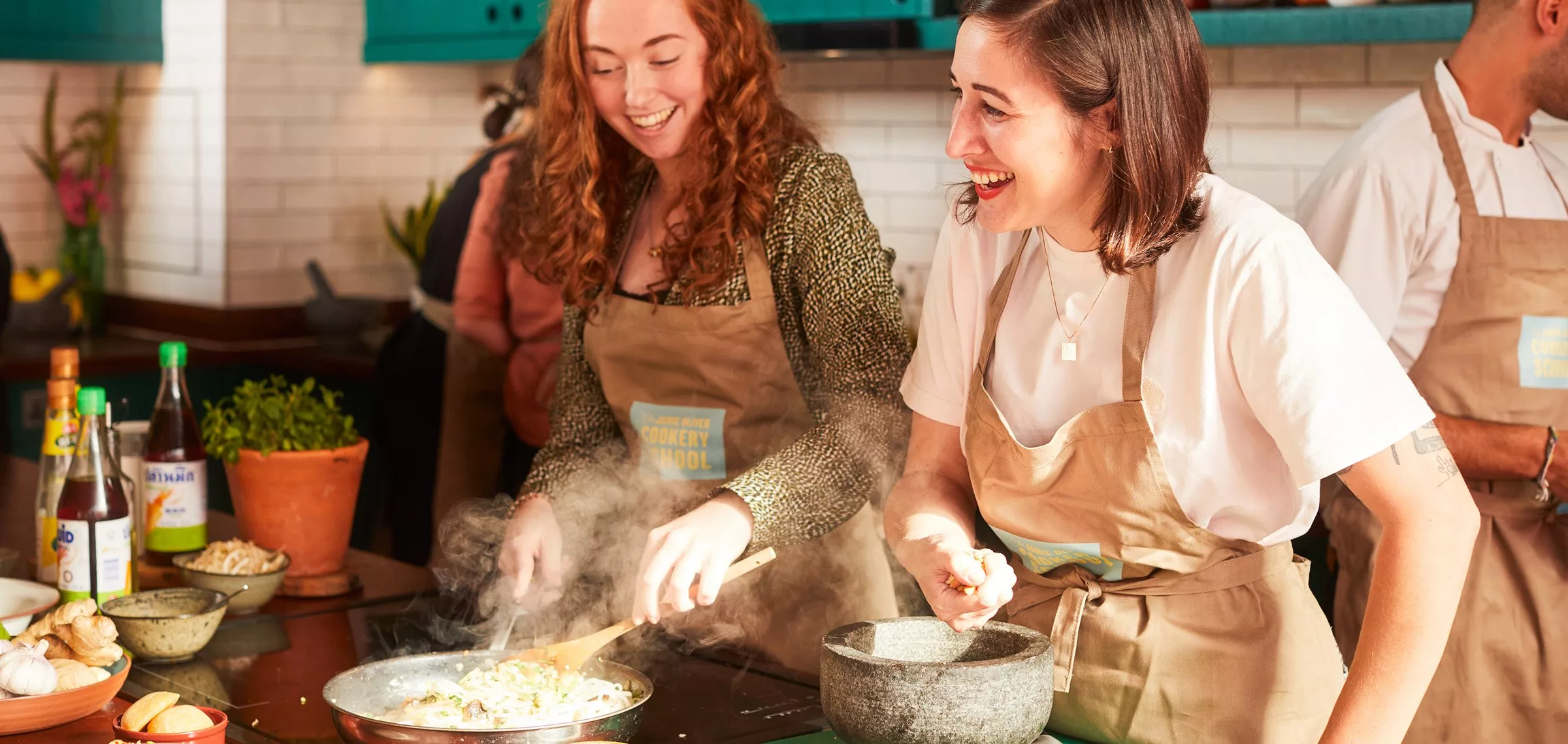 Two people smiling while cooking on a hob