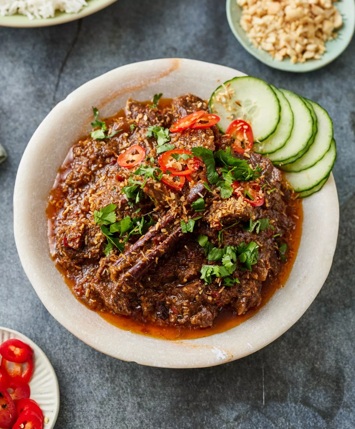 A bowl of beed rendang garnished with coriander, chilli and cucumber