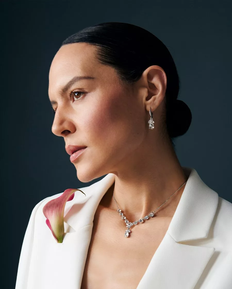Elegant woman in profile wearing diamond jewellery and a white blazer, adorned with a pink calla lily.