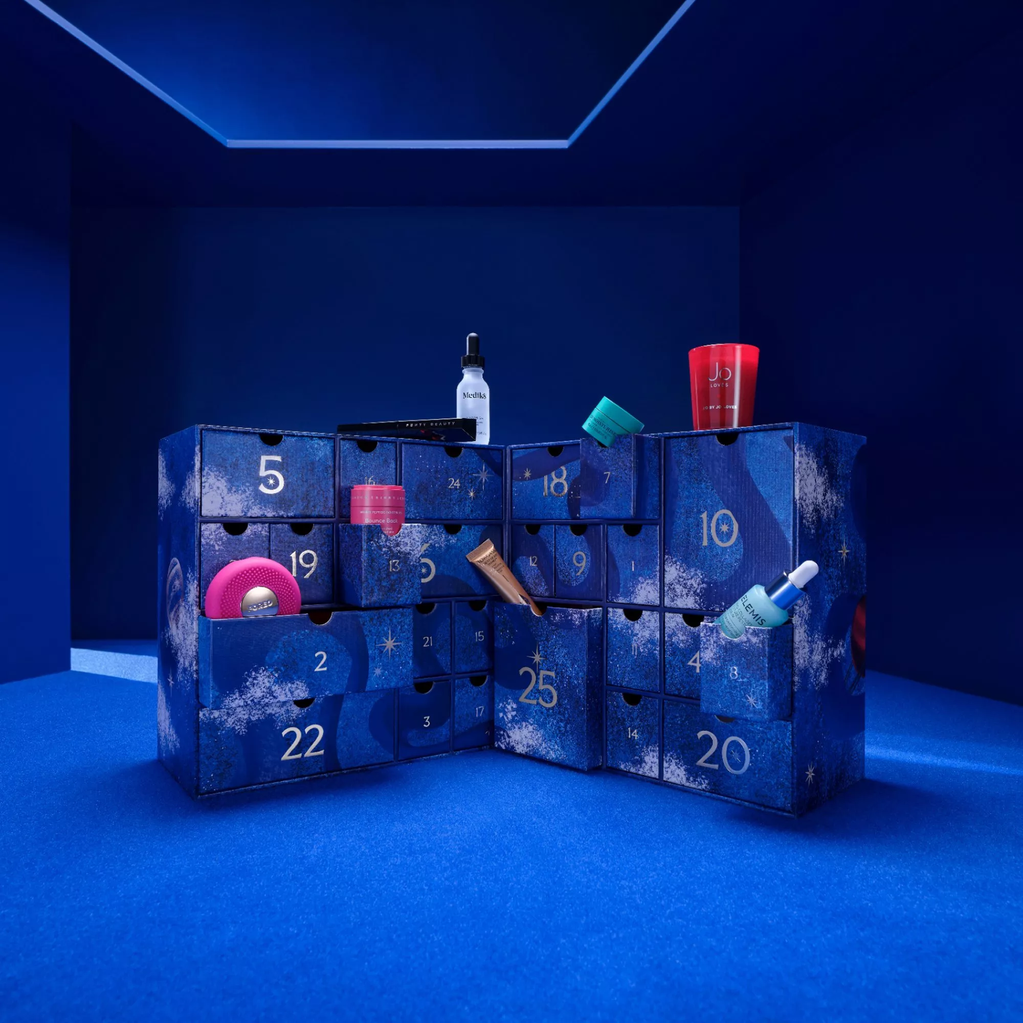 Blue beauty advent calendar with numbered drawers open, displaying skincare bottles, serum dropper and cosmetics on set
