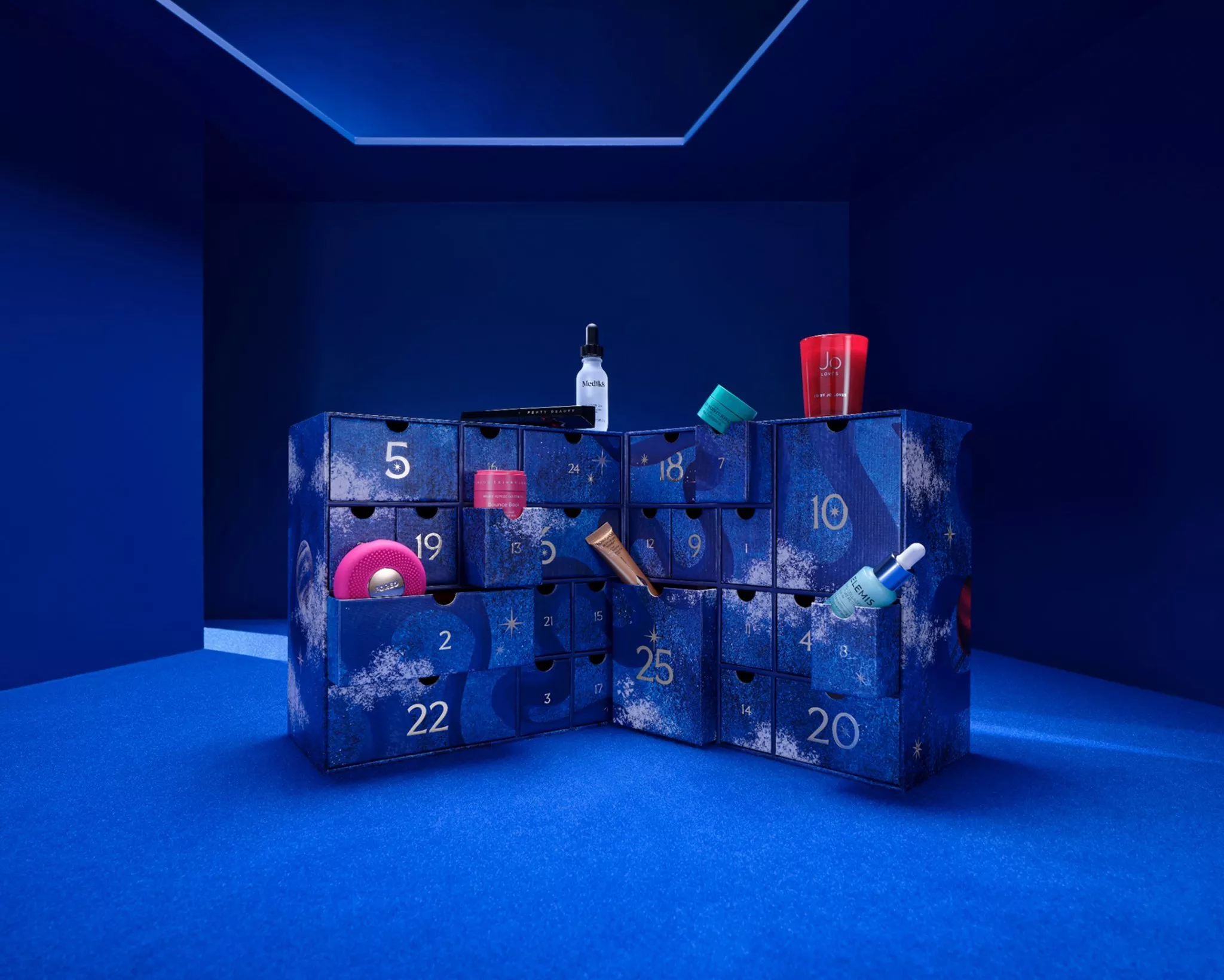 Blue beauty advent calendar gift box with numbered drawers and skincare products on a deep blue studio set