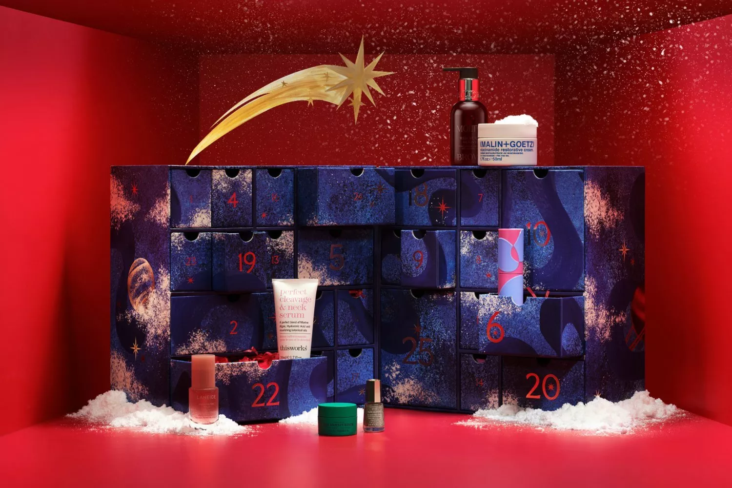 Luxury beauty advent calendar with numbered drawers, skincare products, festive red backdrop and faux snow display