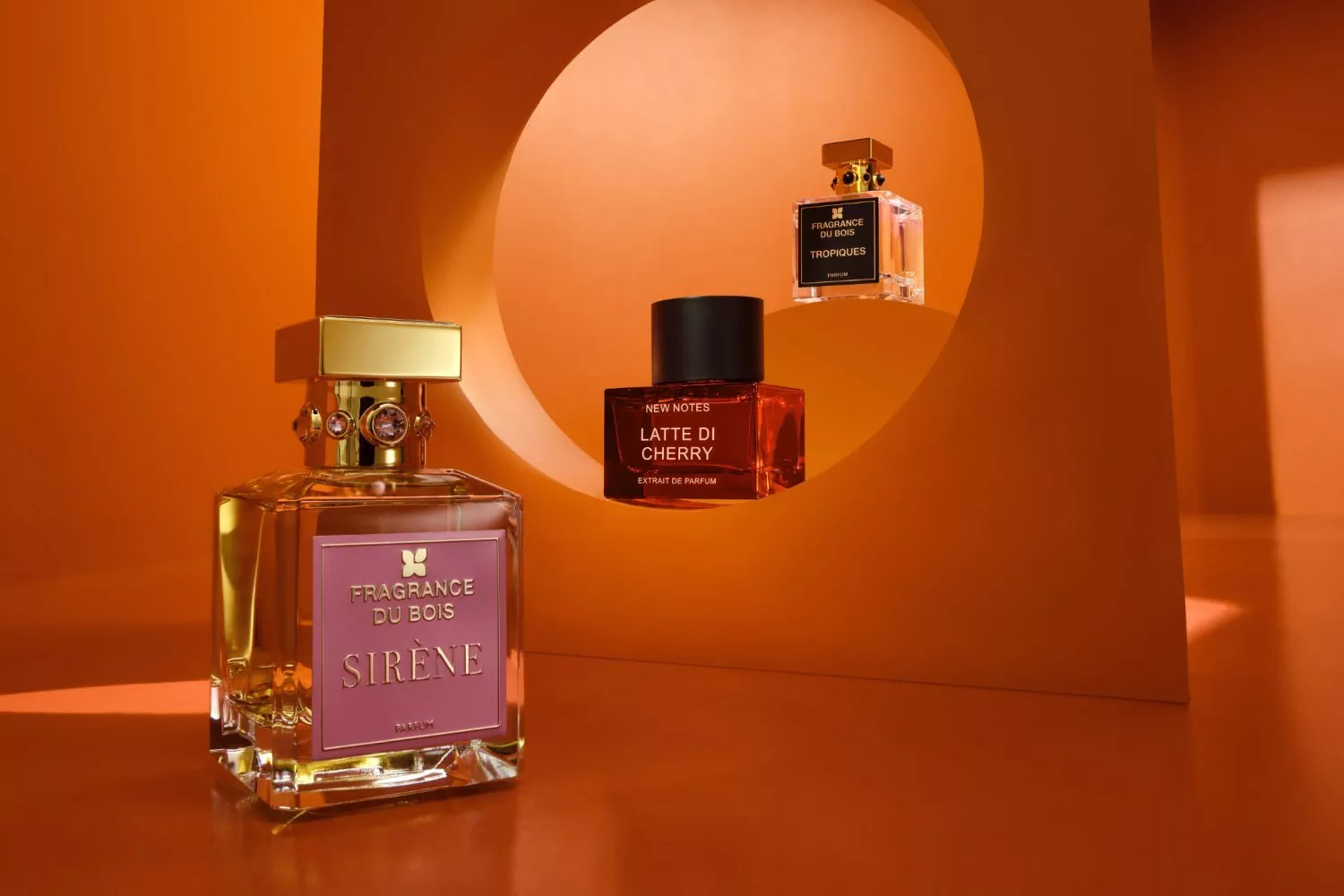 Luxury niche perfume bottles on orange set, featuring Fragrance Du Bois Sirène and New Notes Latte di Cherry